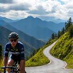 Ciclista profesional ascendiendo una pendiente pronunciada en una carretera colombiana, con un paisaje montañoso vibrante.