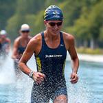 Mujer triatleta saliendo del agua en una carrera de triatlón, con la etapa de ciclismo y carrera de fondo al frente. Enfoque en la transición.